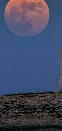 This live wallpaper for phones depicts a tower on top of a hill near a body of water, with a huge super moon in the sky above