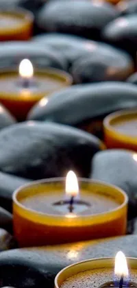 This live wallpaper showcases a stunning group of lit candles resting on top of a pile of rocks