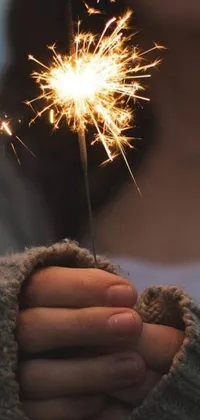 This phone live wallpaper features a illuminating sparkler held by an anonymous person against a dark background