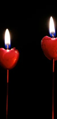 This stunning live phone wallpaper showcases two heart-shaped candles on a black background, creating a striking contrast