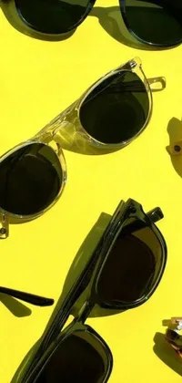 This live wallpaper for your phone features a group of black sunglasses placed on top of a bright yellow surface