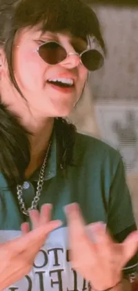 This lively phone live wallpaper features a stylish woman wearing sunglasses and a green shirt, performing a captivating music video with her fingers