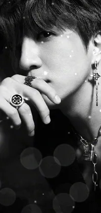 This phone live wallpaper showcases a striking black and white photograph of a person wearing a ring, adorned with multiple medallions