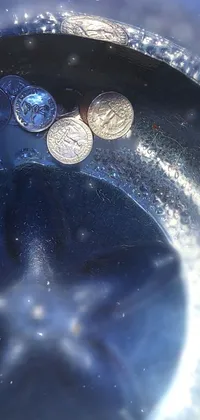 This live wallpaper features a glass filled with glittering coins on a table, set against a blue translucent resin with tones of silver and sapphire