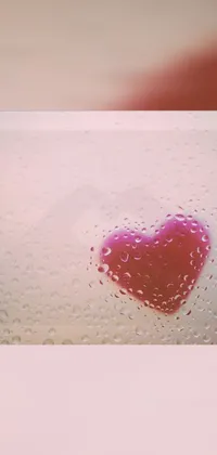 This is a beautiful live wallpaper featuring a bright red heart placed on top of a window that is covered in rain droplets
