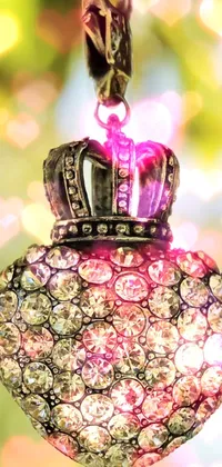 This live phone wallpaper features a beautiful close-up shot of an intricately designed heart and crown amulet hanging from a tree in a lush green forest background