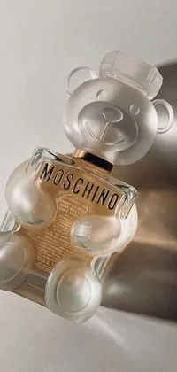 This live wallpaper features a stunningly realistic depiction of a Moschino perfume bottle next to a cuddly teddy bear