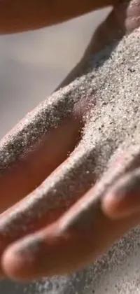 This stunning phone live wallpaper features an up-close shot of a hand holding glistening sand