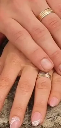 This phone live wallpaper features a close-up of two hands with wedding rings, a blurred background and natural arms, inspired by a famous still-life painter