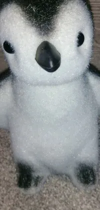 Looking for a cute and unique live phone wallpaper? Check out this design featuring a close-up of a stuffed penguin on a cozy carpet