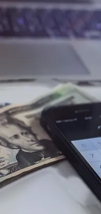 This phone live wallpaper features a sophisticated design with a cell phone resting on a pile of cash, a photo, and a laptop on a desk in the background