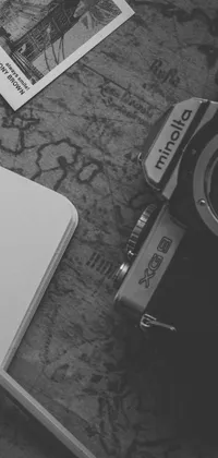 This live phone wallpaper features a stunning black and white photograph of an antique camera and notebook on a textured surface - a beautiful combination of creativity and cherished memories
