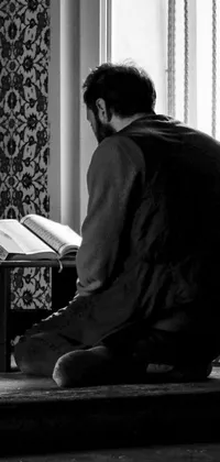 This live phone wallpaper captures a beautiful black and white moment of a person reading a book or religious text