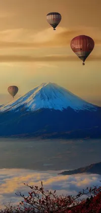 This phone live wallpaper features a group of hot air balloons flying over a mountain landscape, complete with trees, lakes, and small houses