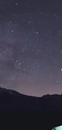 This phone live wallpaper showcases an awe-inspiring view of a starry night sky above serene mountain peaks