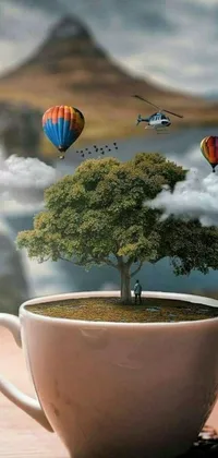 This surrealistic live wallpaper for mobile devices displays a coffee cup on a wooden table, featuring a tree of life inside a glass ball and hot air balloons floating in the sky