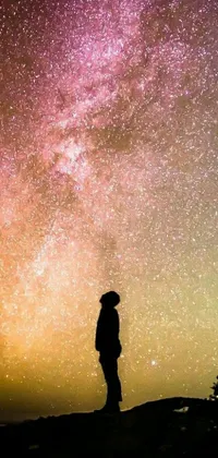 This phone live wallpaper features a stunning scene of a lone figure standing on a hilltop gazing at the stars
