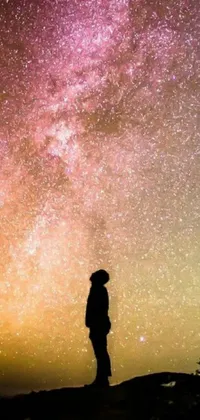 This phone live wallpaper features an awe-inspiring image of a figure standing on top of a hill, gazing up at a sky filled with twinkling stars