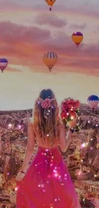 This stunning phone wallpaper features a woman in a pink dress standing by hot air balloons in a lush and dreamy landscape