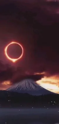 This phone live wallpaper depicts a breathtaking ring of fire set against a mountain backdrop