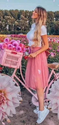 This live wallpaper showcases a woman standing alongside a pink bicycle and surrounded by beautiful flowers in a field
