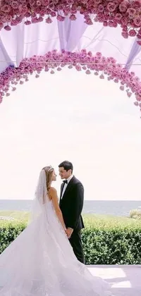 This phone live wallpaper features a beautiful bride and groom standing under a wedding arch adorned with blooming flowers