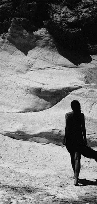 This live phone wallpaper features a striking black and white image of a lone person in a desert cave, carrying a surfboard