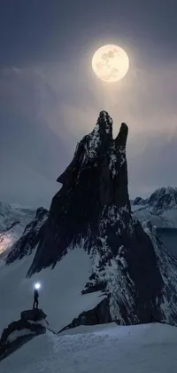 Looking for a spectacular live wallpaper for your phone? Check out this amazing winter wonderland scene! The wallpaper features a man standing on a snow-covered mountain illuminated by a stunning nocturnal moonlight