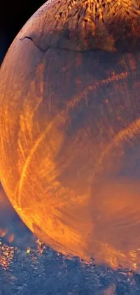 This phone live wallpaper showcases a glass ball resting on snow-covered ground, with an orange spike aura in motion and a golden moon shining in the background