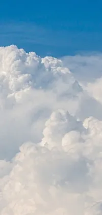 This phone live wallpaper features a breathtaking image of a jetliner soaring through a cloudy blue sky, surrounded by giant cumulonimbus clouds