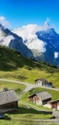 This phone live wallpaper features a group of homes nestled on a lush green hill with towering mountains in the backdrop