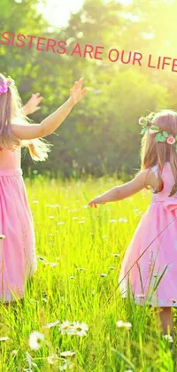 This phone live wallpaper captures two adorable girls in pink standing amidst a green field, designed to evoke peace and love with delicate flowers surrounding them