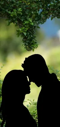 This romantic live wallpaper showcases a striking silhouette of a couple kissing under a tree, against a beautiful greenery backdrop