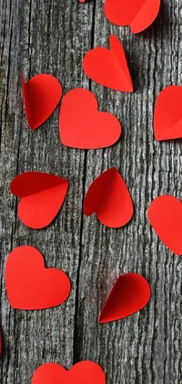 This stunning live wallpaper for phones boasts a charming wooden table adorned with a plethora of red paper hearts and an intriguing photograph