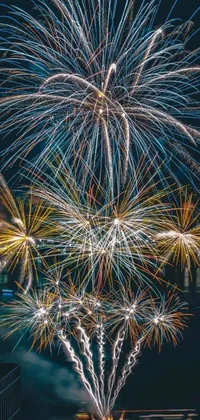This yellow, blue and cyan live iphone wallpaper features beautiful fireworks lighting up the night sky over a body of water