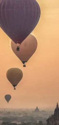 This stunning phone live wallpaper features a group of vibrant hot air balloons floating over a city bathed in warm beige mist