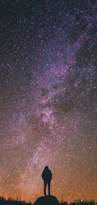 This stunning live wallpaper features a person standing on a hill under a star-filled sky, surrounded by out-of-this-world colors and celestial beauty