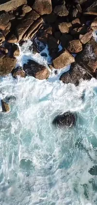 This live wallpaper showcases a serene and peaceful rocky beach landscape where the waves of the sea gently roll in and crash against the rocks