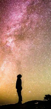 This stunning live phone wallpaper displays an otherworldly scene of a silhouetted spaceman standing atop a hill, admiring a sky full of twinkling stars and mesmerizing pastel colors