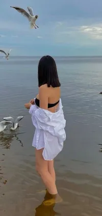 This exquisite phone live wallpaper features a stunning scene of a woman standing in the crystal-clear waters, surrounded by seagulls