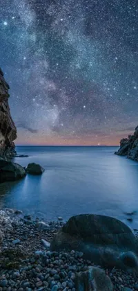 This live wallpaper features a stunning Mediterranean vista of a rocky beach under a starry night sky