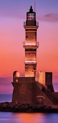 This phone live wallpaper features a picturesque lighthouse standing tall amidst a flowing body of water during a colorful sunset in Old Town Mardin