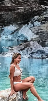 This live wallpaper for your phone features a woman sitting on a rock in the water with a glacier in the background