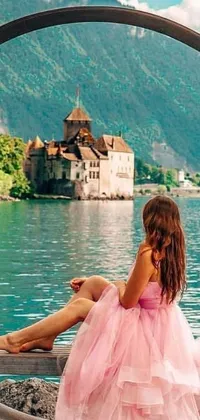 This lively phone wallpaper features a woman in a pink dress sitting on a bench overlooking a serene lake with a boat