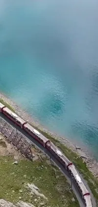 Looking for a stunning live wallpaper to customize your phone screen? Check out this captivating design featuring a long train moving across a steel track near a peaceful body of water