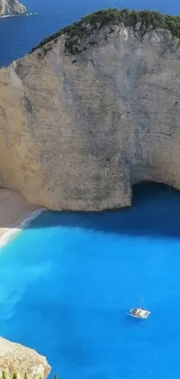 This phone live wallpaper showcases a beautiful body of water juxtaposed to a sandy beach fringed by green foliage and steep cliffs