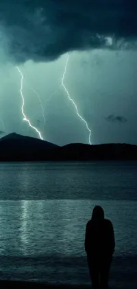 This phone live wallpaper showcases a lone figure, surrounded by thunderstorms and lightning bolts, standing in front of a serene body of water