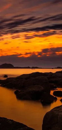 This live wallpaper portrays a captivating sunset over a peaceful body of water, marked by rocks in the foreground and captured in stunning detail