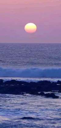 This phone live wallpaper depicts a stunning sunset over the ocean, with a surfer paddling in the water and a large wave approaching the shore
