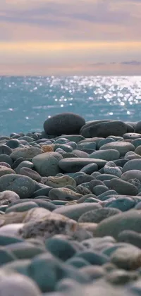 This stunning phone live wallpaper features a serene scene of rocks resting on a calm teal-streaked beach next to the ocean